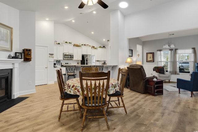 dining room featuring ceiling fan with notable chandelier, high vaulted ceiling, and light wood-type flooring