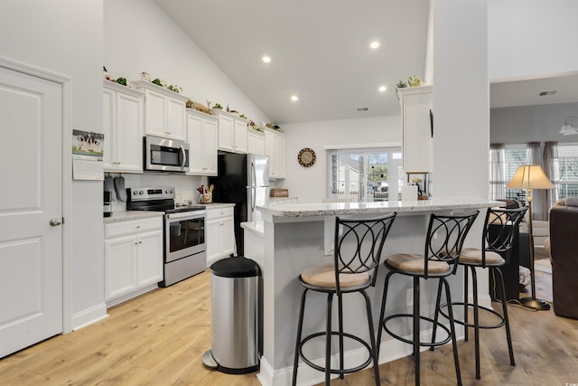 kitchen featuring light stone countertops, a kitchen breakfast bar, white cabinets, and appliances with stainless steel finishes