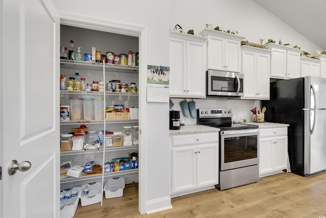 kitchen with white cabinetry, light wood-type flooring, lofted ceiling, and appliances with stainless steel finishes