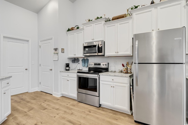 kitchen with stainless steel appliances, light stone countertops, light hardwood / wood-style floors, and white cabinets