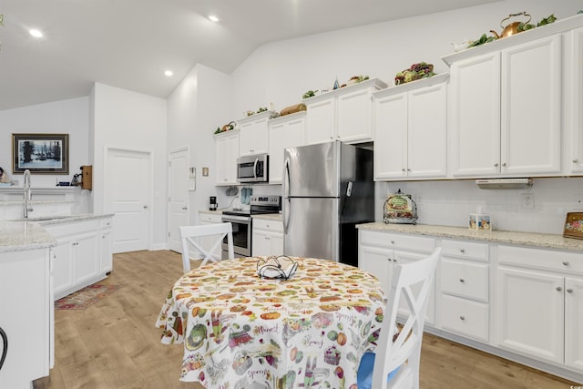 kitchen with stainless steel appliances, vaulted ceiling, light stone countertops, and sink