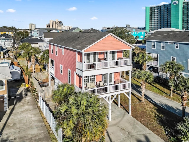 exterior space featuring concrete driveway, a shingled roof, a balcony, and a city view