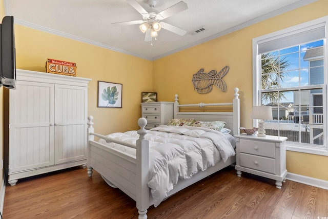 bedroom featuring wood finished floors, a ceiling fan, visible vents, baseboards, and ornamental molding