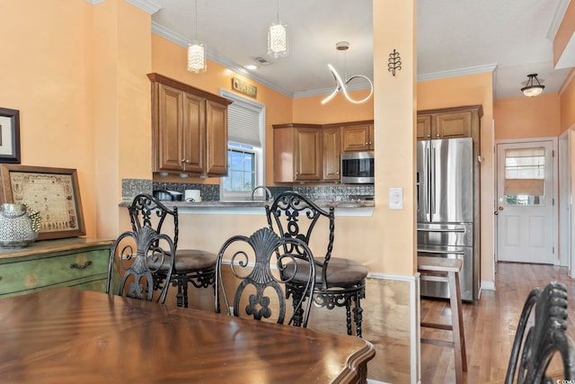 kitchen with stainless steel appliances, brown cabinetry, crown molding, and tasteful backsplash