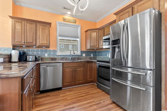 kitchen featuring stainless steel appliances, brown cabinetry, a sink, and ornamental molding