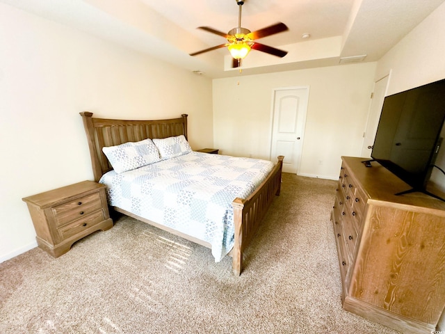 bedroom with light colored carpet, a raised ceiling, and ceiling fan