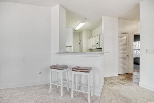 kitchen featuring white cabinetry, light carpet, a kitchen breakfast bar, and kitchen peninsula