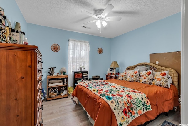 bedroom with ceiling fan, light hardwood / wood-style floors, and a textured ceiling