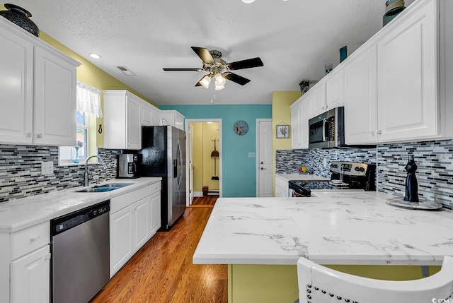 kitchen with appliances with stainless steel finishes, white cabinetry, sink, ceiling fan, and light hardwood / wood-style flooring