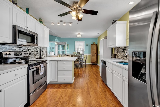 kitchen featuring appliances with stainless steel finishes, white cabinetry, light hardwood / wood-style floors, decorative backsplash, and kitchen peninsula