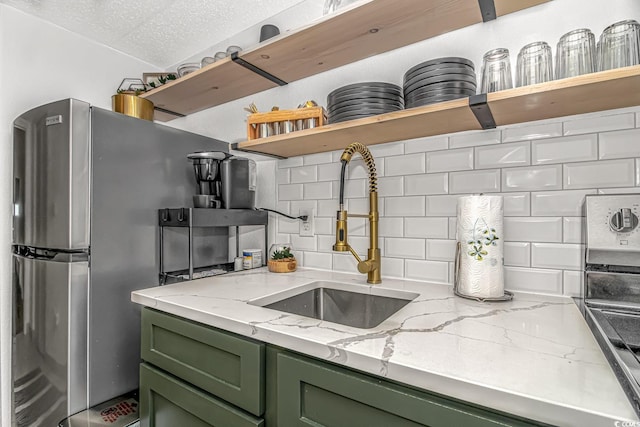 kitchen with tasteful backsplash, green cabinetry, light stone countertops, and sink