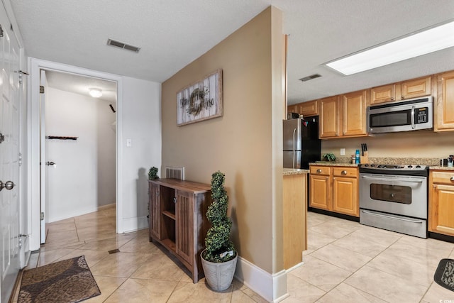 kitchen with light tile patterned floors, stainless steel appliances, a textured ceiling, and light stone countertops