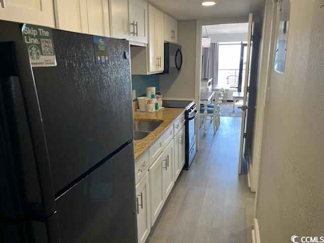 kitchen featuring black appliances, white cabinetry, decorative backsplash, and light wood-style floors