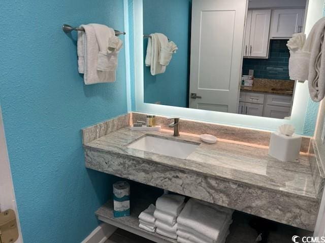 bathroom with a textured wall, vanity, and decorative backsplash