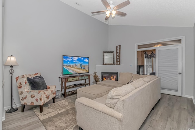 living room featuring light wood-style floors, lofted ceiling, a glass covered fireplace, and ceiling fan