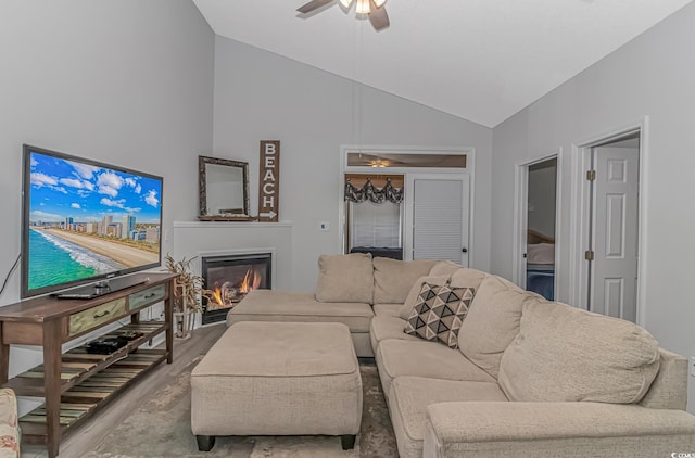 living area with light wood-style floors, ceiling fan, high vaulted ceiling, and a glass covered fireplace