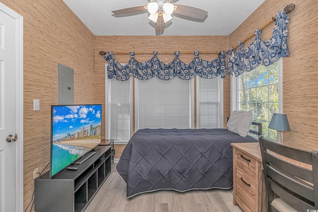 bedroom with a textured ceiling, ceiling fan, electric panel, and light wood-style floors