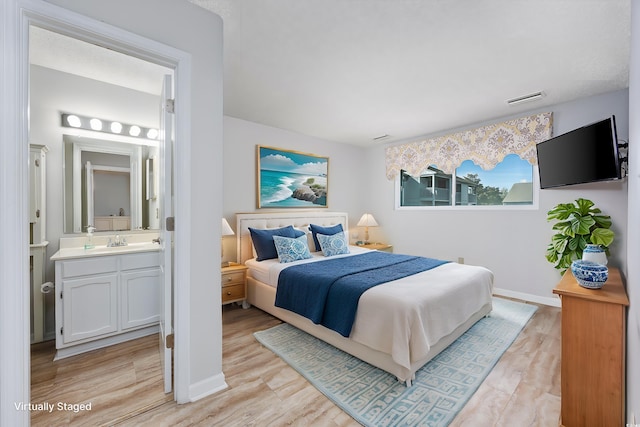 bedroom with ensuite bathroom, sink, and light wood-type flooring