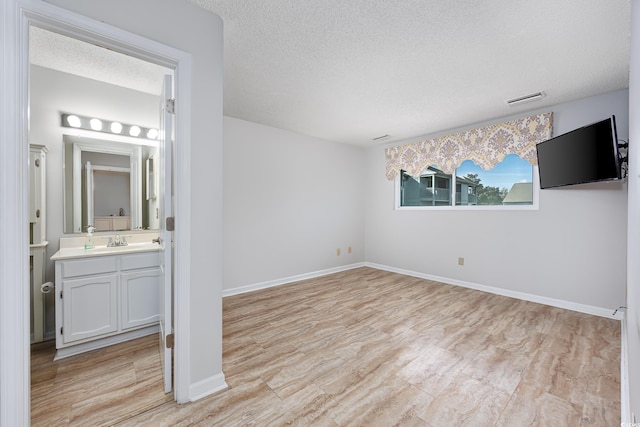 unfurnished room featuring sink, a textured ceiling, and light hardwood / wood-style flooring