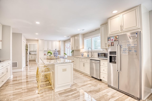 kitchen featuring sink, stainless steel appliances, a center island, light stone countertops, and a kitchen bar