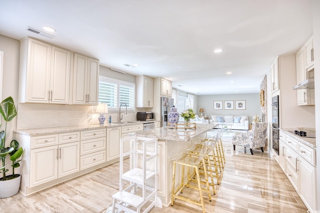 kitchen featuring sink, a kitchen bar, light stone countertops, black appliances, and a kitchen island