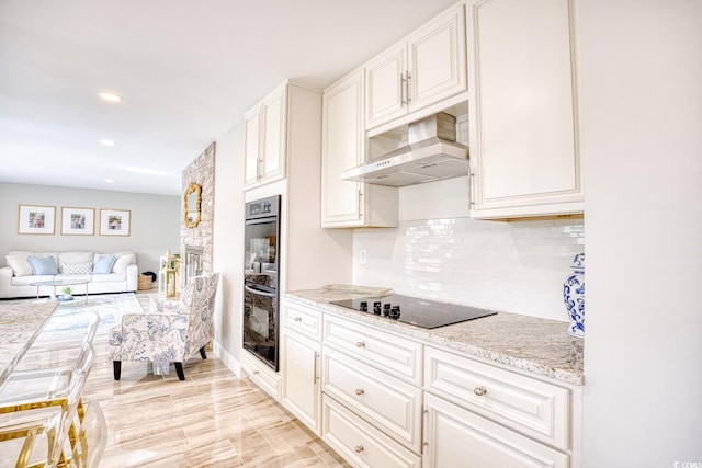 kitchen featuring white cabinets, decorative backsplash, light stone counters, black appliances, and wall chimney exhaust hood