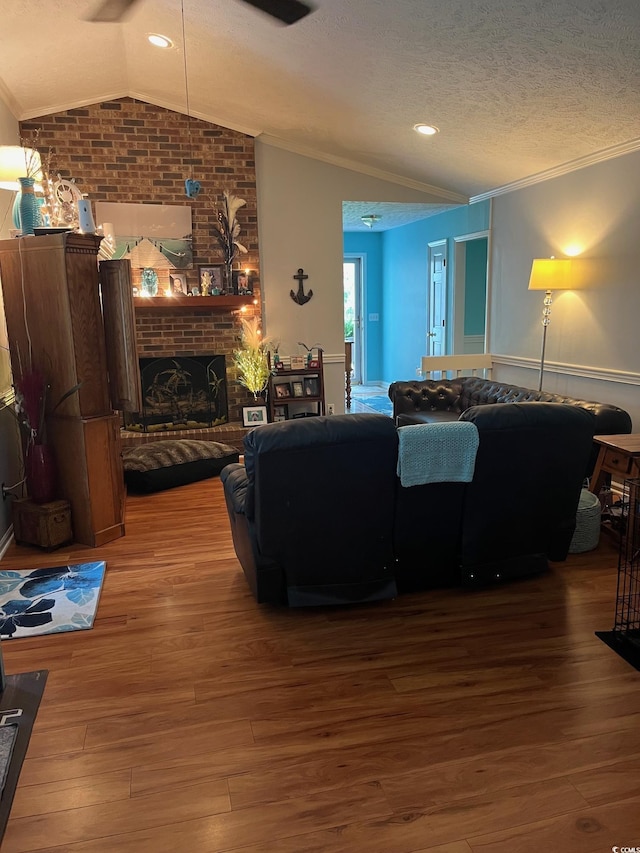 living room with hardwood / wood-style flooring, a fireplace, ornamental molding, a textured ceiling, and vaulted ceiling