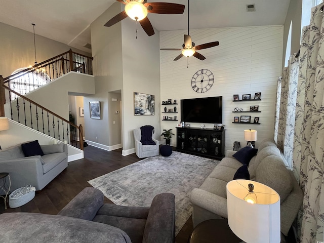 living room featuring dark wood-type flooring, a towering ceiling, and ceiling fan with notable chandelier