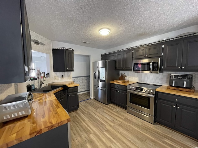 kitchen featuring butcher block counters, sink, a textured ceiling, light wood-type flooring, and appliances with stainless steel finishes