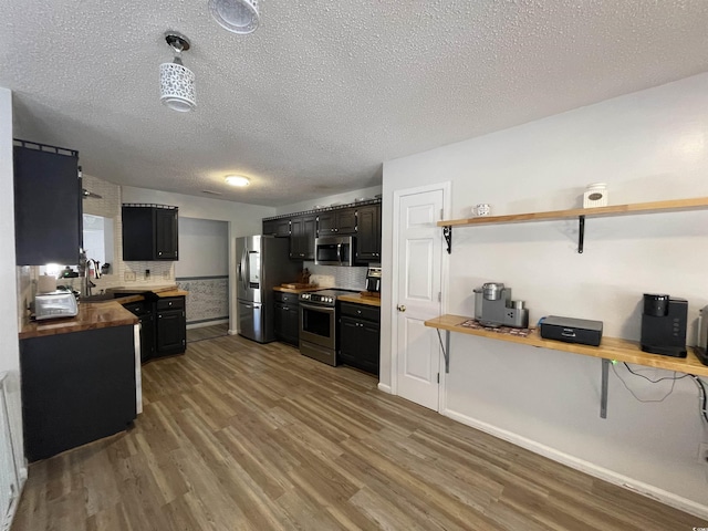 kitchen featuring tasteful backsplash, wood-type flooring, wooden counters, stainless steel appliances, and a textured ceiling