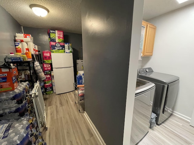 washroom featuring light wood-type flooring, a textured ceiling, and washer and clothes dryer