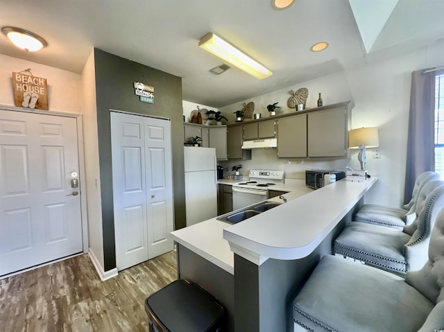 kitchen with a breakfast bar, sink, light hardwood / wood-style floors, kitchen peninsula, and white appliances