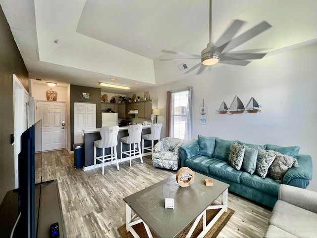 living room featuring light hardwood / wood-style flooring, a raised ceiling, and ceiling fan