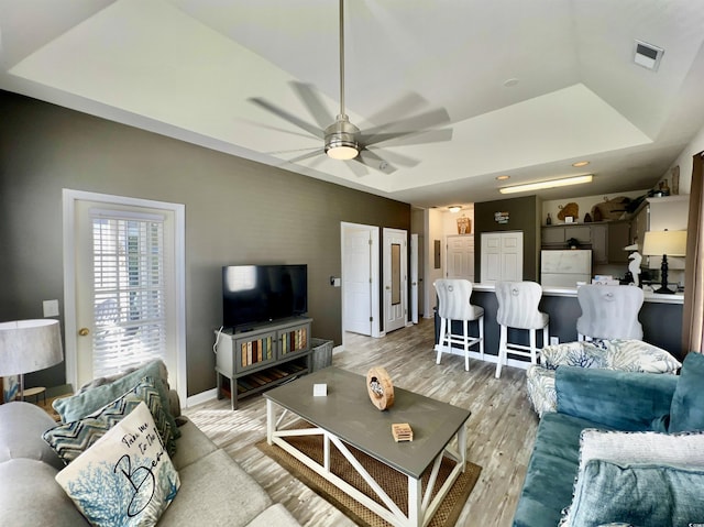 living room featuring ceiling fan, light hardwood / wood-style floors, and a tray ceiling