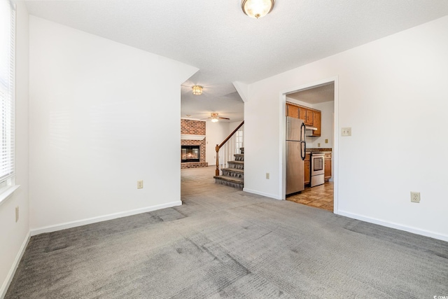 carpeted spare room featuring ceiling fan, a fireplace, and a textured ceiling