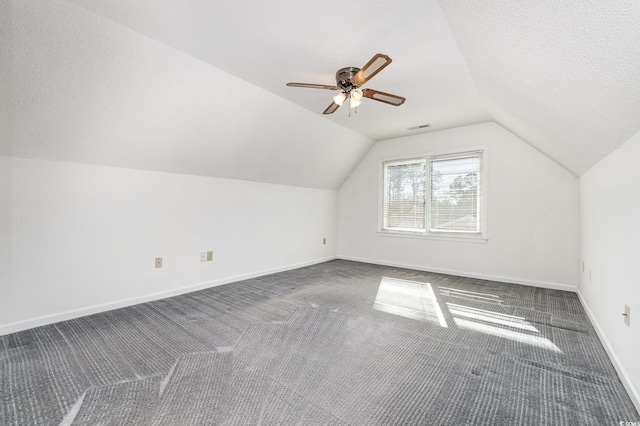 additional living space featuring ceiling fan, vaulted ceiling, a textured ceiling, and dark colored carpet