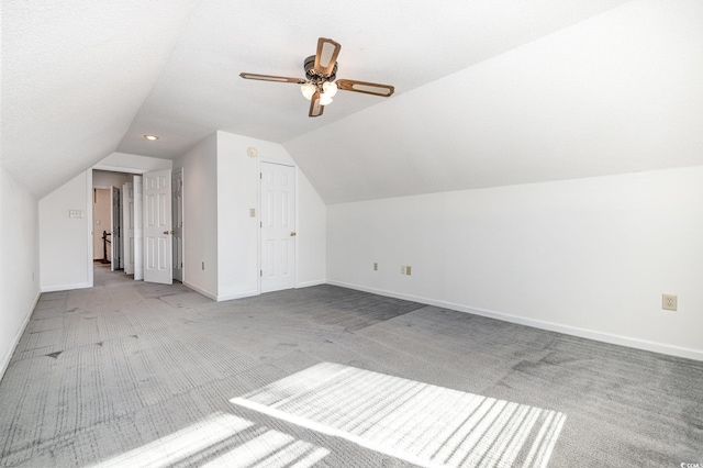 additional living space with vaulted ceiling, light carpet, a textured ceiling, and ceiling fan