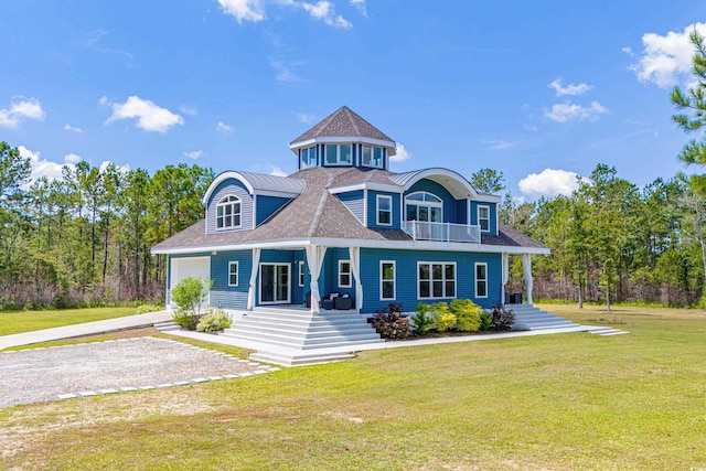 shingle-style home with driveway, a balcony, an attached garage, covered porch, and a front yard