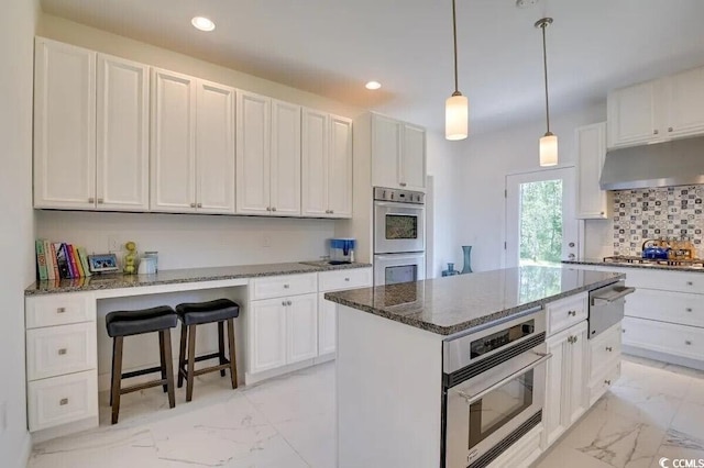 kitchen featuring under cabinet range hood, stainless steel appliances, marble finish floor, decorative backsplash, and a warming drawer