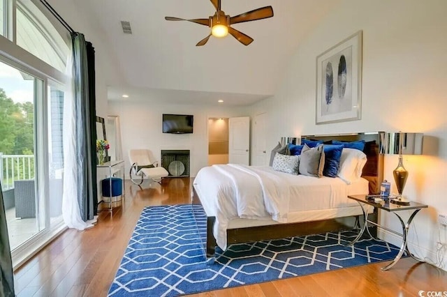 bedroom with visible vents, a towering ceiling, wood finished floors, access to outside, and a fireplace