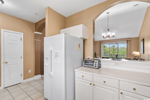 kitchen with light tile patterned flooring, white fridge with ice dispenser, hanging light fixtures, a notable chandelier, and white cabinets