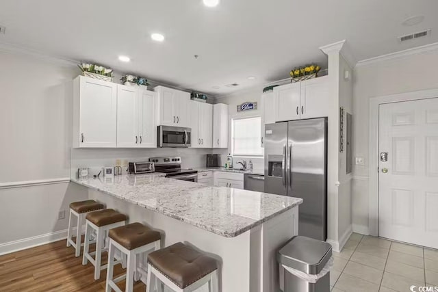 kitchen featuring appliances with stainless steel finishes, white cabinets, a kitchen bar, ornamental molding, and kitchen peninsula