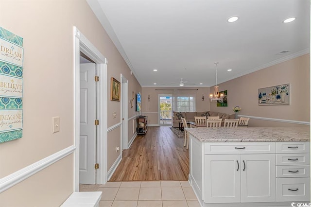 kitchen with white cabinetry, light stone counters, light tile patterned floors, ornamental molding, and ceiling fan with notable chandelier