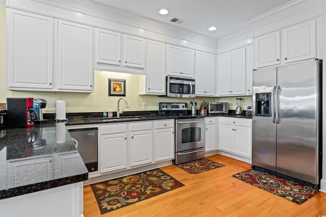 kitchen featuring sink, dark stone countertops, white cabinets, stainless steel appliances, and light hardwood / wood-style flooring