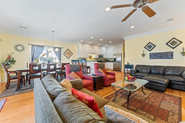 living room with ornamental molding, ceiling fan with notable chandelier, and light wood-type flooring