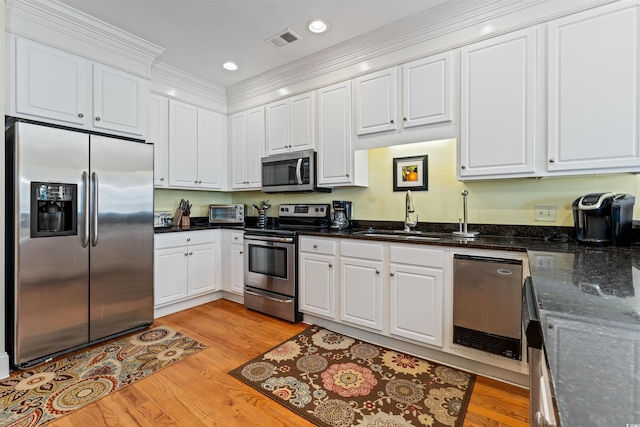 kitchen featuring appliances with stainless steel finishes, white cabinetry, sink, dark stone counters, and light wood-type flooring