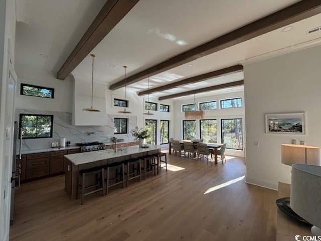 kitchen featuring hanging light fixtures, beam ceiling, a center island with sink, a kitchen bar, and dark hardwood / wood-style flooring