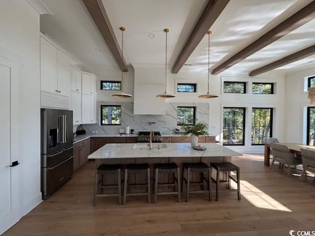 kitchen featuring a breakfast bar, hanging light fixtures, high quality fridge, an island with sink, and white cabinets