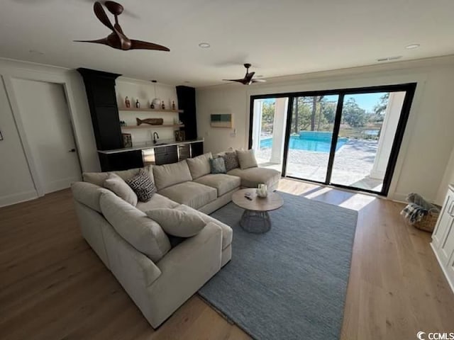 living room with ceiling fan, ornamental molding, light hardwood / wood-style floors, and indoor wet bar