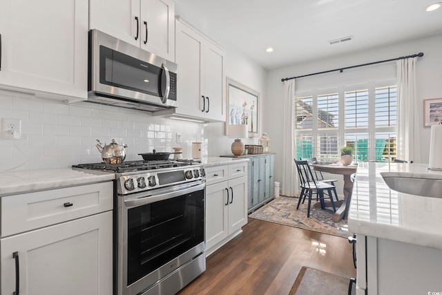 kitchen with appliances with stainless steel finishes, tasteful backsplash, white cabinets, dark hardwood / wood-style flooring, and light stone counters